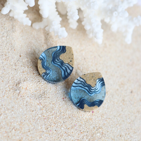 Small dark blue resin earrings on sand