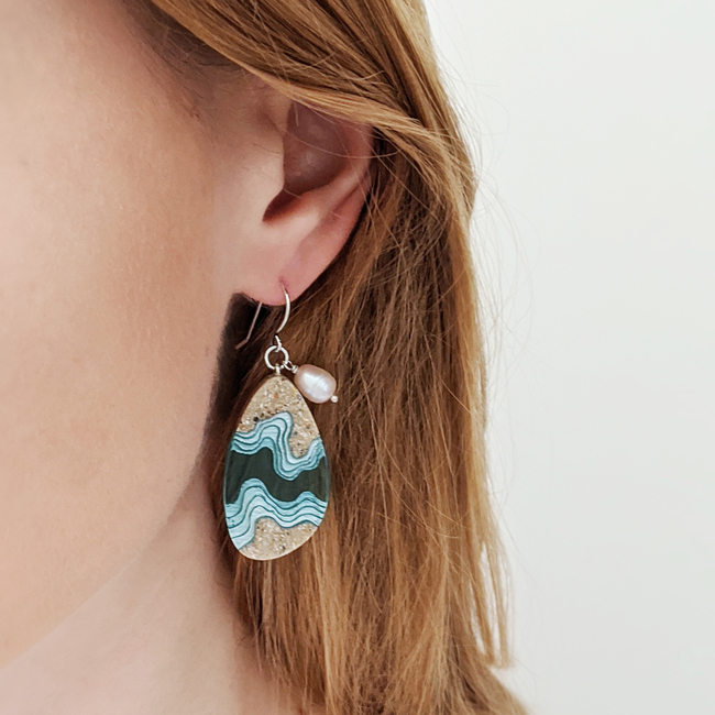 Rockpool large beach sand and blue resin dangle earrings on model left.