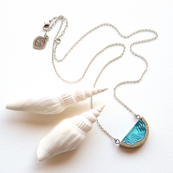 Dainty beach sand and dark blue resin necklace with white background and shells